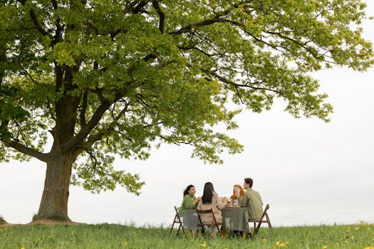 Friends enjoying a picnic under a large oak tree outdoors on a sunny day.